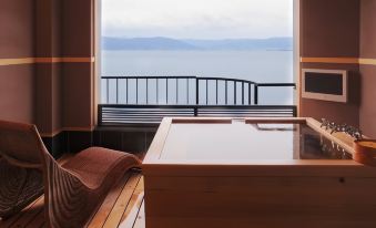 a modern living room with a large window offering a view of the ocean , and a wooden bench in front of a wooden table at Kamisuwa Onsen Shinyu