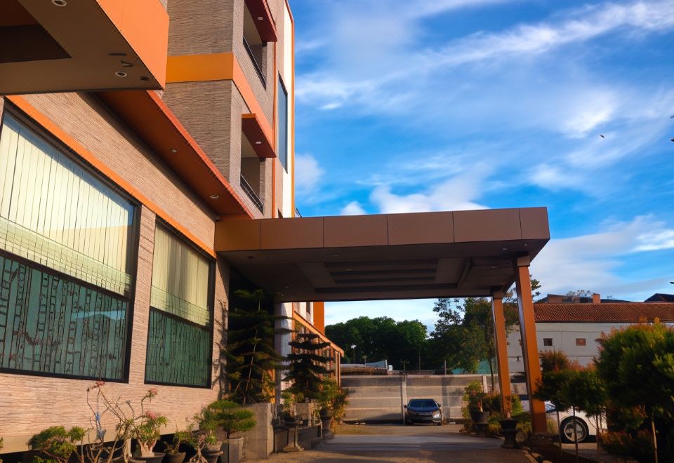 a parking lot with a car parked in front of a building , surrounded by trees at Grand Krakatau Hotel Serang