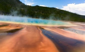 a beautiful landscape with a hot spring and steam rising from it , surrounded by mountains at Yellowstone Park Hotel