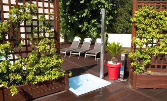 a wooden deck with several lounge chairs and a red bucket filled with water , surrounded by lush greenery at Hotel Concorde