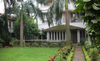 a white house surrounded by a lush green garden , with palm trees in the background at Hotel East Coast