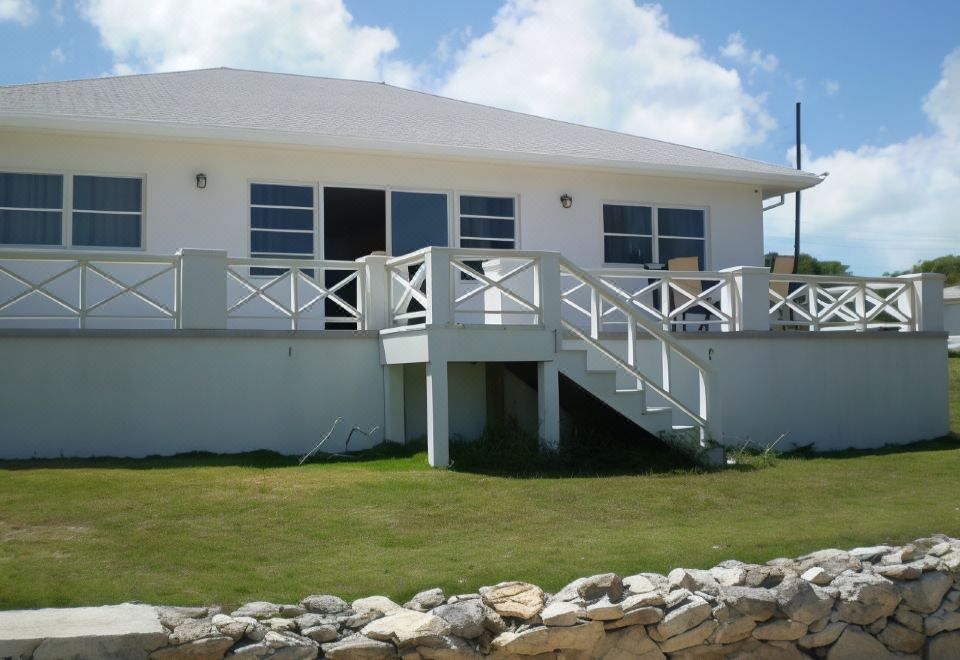 a white house with a stone wall and wooden stairs leading up to it , surrounded by green grass at Cottage Cut Villas