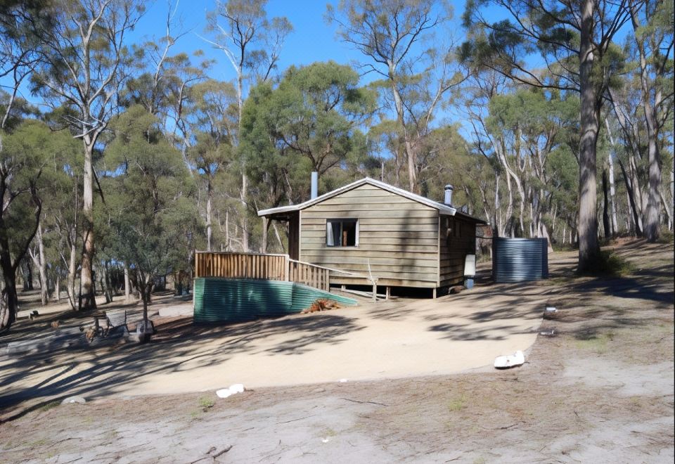 a small wooden cabin surrounded by trees , with a green fence surrounding the property and a small swimming pool in the background at Gumleaves Bush Holidays