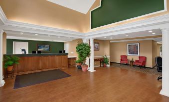 a spacious lobby with wooden floors , high ceilings , and multiple seating areas , including a reception desk , red armchairs , and green ceiling accents at Comfort Inn