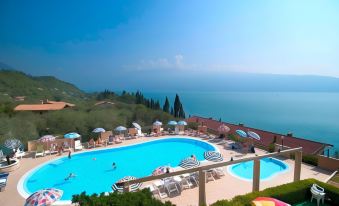 a large outdoor swimming pool surrounded by lounge chairs and umbrellas , with a view of the ocean in the background at All Inclusive Hotel Piccolo Paradiso