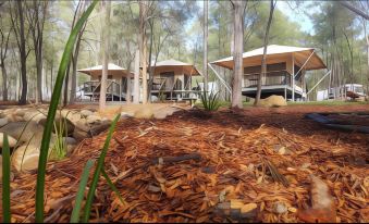 a group of small wooden houses surrounded by trees and grass , with a pile of wood in the foreground at Paradise Country Farmstay