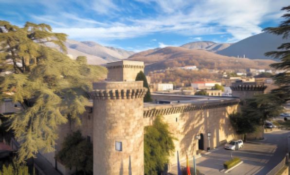 a large stone building with a tower is surrounded by trees and mountains in the background at Parador de Jarandilla