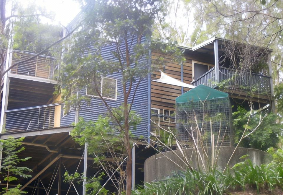 a wooden house with a blue exterior is surrounded by trees and has a green umbrella in the foreground at Tambaridge Bed & Breakfast