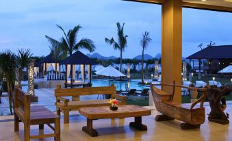 a large window overlooking a patio with wooden furniture and palm trees , creating a tropical atmosphere at The Jayakarta Suites Komodo Flores