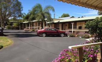 a red car is parked in front of a two - story motel with palm trees and flowers at Oasis Motel