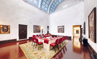 a large dining room with a long table surrounded by red chairs and a painting on the wall at Convento do Espinheiro, Historic Hotel & Spa