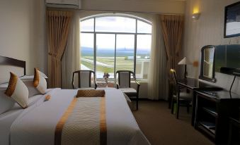 a large bed with a white and gold blanket is in the middle of a room with a window overlooking an ocean at Indochine Hotel