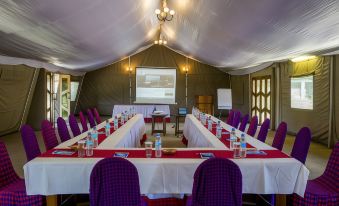 a conference room with a long table set for a meeting , surrounded by chairs and a projector screen at Ngorongoro Serena Safari Lodge