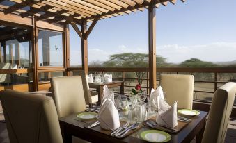 a table is set with plates , silverware , and napkins on a wooden deck overlooking a mountainous landscape at Seronera Wildlife Lodge