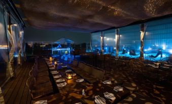 an empty rooftop bar with multiple dining tables , chairs , and a large mirror reflecting the night sky at Kos Pilar Hotel