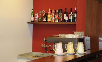 a bar counter with various bottles of alcohol , cups , and other items on it , along with a red wall in the background at Hotel California