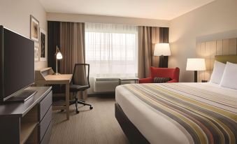 a modern hotel room with a bed , desk , and window , as well as a red chair and lamps at Country Inn & Suites by Radisson, Ft. Atkinson, WI