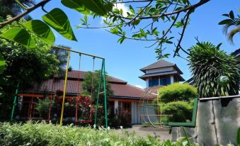 a house with a playground in front of it , surrounded by trees and grass , under a blue sky at Front One Resort Magelang