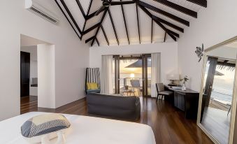 a modern bedroom with a black bed , white walls , and a view of the ocean through a window at Noku Maldives