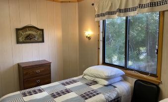 a bedroom with a bed , nightstand , and window with curtains , as well as a black chair and window sill at Betsie Riverside Resort