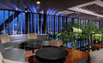 a modern living room with a large flat - screen tv mounted on the wall , surrounded by couches and chairs at Aston Imperial Bekasi Hotel & Conference Center