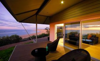 a wooden deck overlooking the ocean , with several chairs placed on the deck for relaxation at Eco Beach Wilderness Retreat