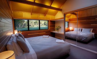 a cozy bedroom with a large bed , a mirror , and a view of trees outside the window at Girraween Environmental Lodge