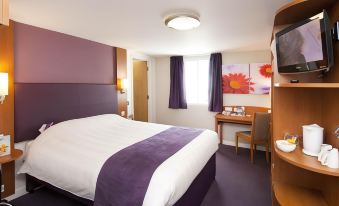 a hotel room with a purple and white bed , a desk , a chair , and a television at Premier Inn Derby East