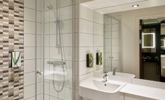 a modern bathroom with a white sink and shower area , illuminated by a wall - mounted mirror at Premier Inn Lichfield North East (A38)