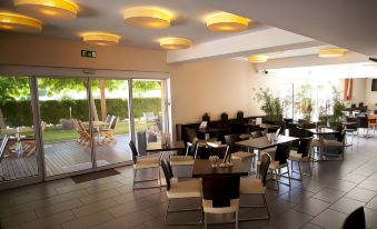 a modern restaurant with wooden floors , white walls , and a balcony overlooking a garden , featuring comfortable dining tables and chairs at Ahotel Ljubljana