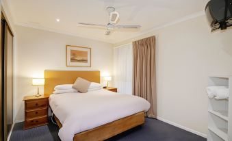 a well - decorated hotel room with a large bed , white walls , and a ceiling fan , along with a window and curtains at Parkwood Motel & Apartments