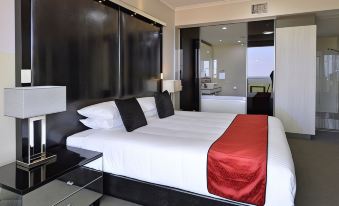 a large bed with white linens and a red blanket is in a room with a glass door at Rydges Palmerston - Darwin, an EVT hotel