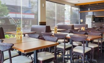 a restaurant with wooden tables and chairs , white cushions on the chairs , and large windows at Alpha Inn