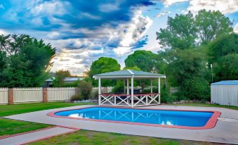 a backyard with a pool , surrounded by green grass and trees , under a cloudy sky at Rest Point Motor Inn