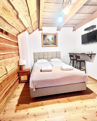 a cozy bedroom with a wooden floor , a bed with pink linens , and a television mounted on the wall at Troll