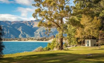 a serene landscape of a lake surrounded by trees , with mountains in the background and a clear blue sky above at The Camp - Lake Hawea