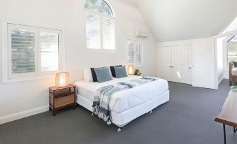 a white bedroom with a large bed , two nightstands , and a window , all lit by two lamps at BreakFree Raffertys Beach Resort