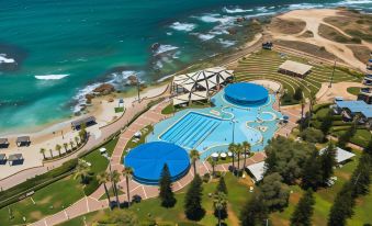aerial view of a resort with a large pool surrounded by grass , trees , and ocean in the background at Resort Hadera by Jacob Hotels