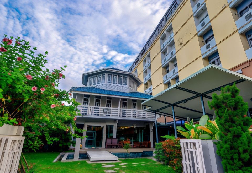 a modern building with a curved design , surrounded by lush greenery and flowers , under a blue sky with scattered clouds at Viva Hotel Songkhla