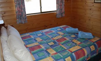 a bed with a colorful quilt is situated in a room with wooden walls and window curtains at Gumleaves Bush Holidays