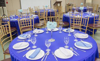 a round table is set with white plates , blue napkins , and wine glasses in a room at Eurotel Angeles