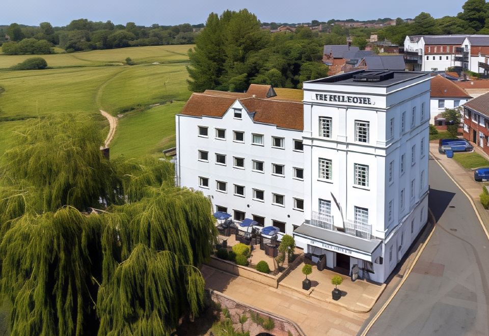 aerial view of a white hotel building surrounded by trees , with a golf course in the background at The Mill Hotel