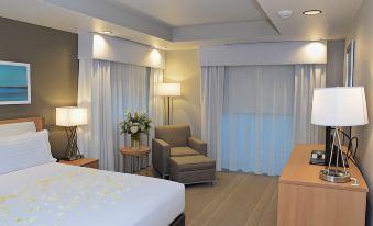 a modern hotel room with white walls , wooden floors , and large windows , featuring a bed , couch , nightstand , lamp , and bed at Holiday Inn Cincinnati N - West Chester