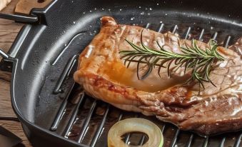 a close - up image of a piece of meat with a sprig of rosemary on top , placed on a grill at BlissWood B&B Ranch