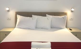 a neatly made bed with a red blanket and white pillows , topped with a pillow and a key at Academy Hotel