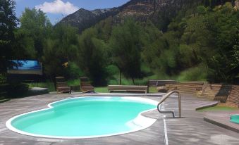 a large swimming pool surrounded by wooden decking , with a mountain in the background and a hot tub on the side at Diamond J Ranch