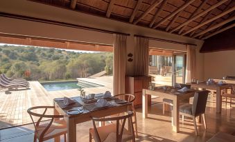 a dining room with a table set for a meal and a view of a swimming pool outside at Bukela Game Lodge - Amakhala Game Reserve