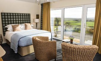 a cozy bedroom with a large bed , two chairs , and a balcony overlooking a grassy field at Peartree Hill