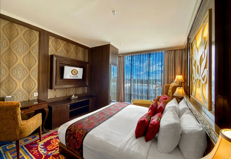 a large bed with a white comforter and red pillows is in a room with a television , desk , and window at Sapphire Sky Hotel & Conference
