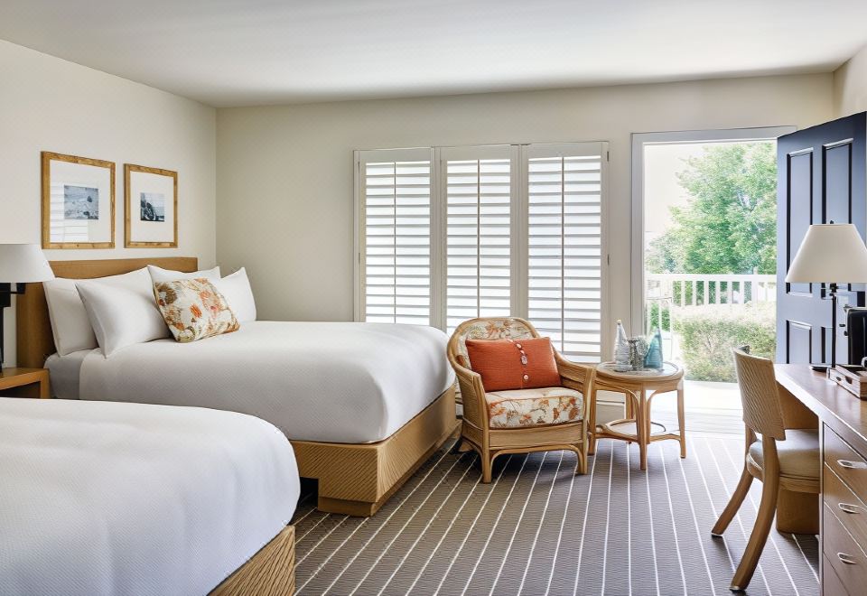 a hotel room with two beds , a chair , and a window overlooking a balcony , all decorated in white at Hotel Carmel